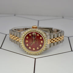Luxury Rolex Ladies Datejust 26mm red dial watch featuring 2ct diamond bezel and two-tone Jubilee bracelet, displayed on geometric tile surface.